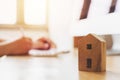 Close up wooden toy house with hand signing loan document to home ownership