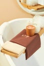 Close-up of a wooden tray placed across the bathtub with cloth towels, pink salt, scented candles and a bath sponge. Space with Royalty Free Stock Photo