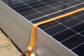 Close-up of a worker\'s hands tying a stack of solar panels with orange webbing