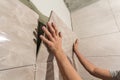 Close-up of worker tiler hands installing light beige ceramic tiles on walls of future bathroom. Tiles installation, home