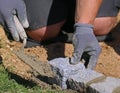 Close up of worker with trowel and gloves, laying a lawn edge massive granite blocks as a part of garden limitation