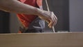 Close up of a workman in coverall applying glue with a brush inside the hole of a wooden beam on blurred background