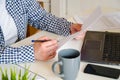 Close-up workspace: laptop, coffee cup, phone. Female hands take notes on white sheet of paper Royalty Free Stock Photo