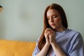 Close-up of worried anxious young red-haired woman sitting on couch praying god with folded hands having life crisis. Royalty Free Stock Photo