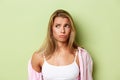 Close-up of worried blond woman in pink shirt, looking at upper left corner and sulking sad, standing over green