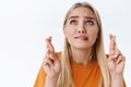 Close-up worried, very nervous blond caucasian woman in orange t-shirt, fingers crossed hope god hear prayers as furrow