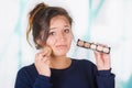 Close up of worried young woman holding a make up palette and doing crazy make-up in her face using a sponge, in a