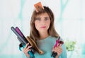 Close up of a worried young woman wearing a hair roller in ther head and holding in the hands a straighteners and set of