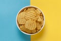 Close up of Wrinkled Wavy Potato Chips in white ceramic bowl, Popular Ready to eat crunchy, salty pale-yellow color over blue Royalty Free Stock Photo