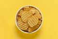 Close up of Wrinkled Wavy Potato Chips in white ceramic bowl, Popular Ready to eat crunchy, salty pale-yellow color over yellow Royalty Free Stock Photo