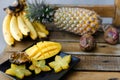 Close up yellow mango with carambola on plate near pine-apple and bananas on wooden table.