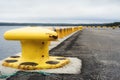 Close-up of yellow metallic mooring column or bollard on the edge of stone quay blue water background. Marine Bollard Royalty Free Stock Photo