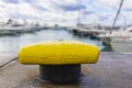 Close-up of a yellow mooring iron bollard. In front of blurry yachts at sea