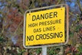 Close up of a yellow outdoor warning sign saying dager high pressure gas line no crossing