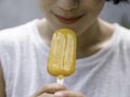 Yellow popsicle in happy smiling beautiful Asian woman`s hand. Royalty Free Stock Photo