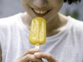 Yellow popsicle in happy smiling beautiful Asian woman`s hand. Royalty Free Stock Photo