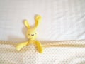 Close up yellow rabbit doll laying on white bed under cream blanket pink polka dot pattern Royalty Free Stock Photo