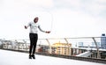 Young active black sportsman skipping with a rope in a city, wearing hoodie.