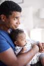 Close up of young adult African American father sitting in an armchair holding his three month old baby son, side view, waist up,