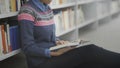 Close up of Young african american woman is reading book sitting on floor in university library. Royalty Free Stock Photo