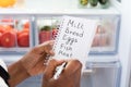 Woman Writing On Shopping List Near Refrigerator