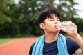 Close up young Asian teenages drinking water from bottle after run in park with copy space