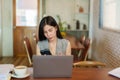 Close-up young Asian woman sitting on mobile phone, while resting eyes from work, looked at laptop screen on desk in front Royalty Free Stock Photo