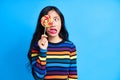 Close up of young asian woman sticking out tongue to colorful lollipop isolated on blue background Royalty Free Stock Photo