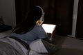 Close up of young Asian woman watching series with tablet and headphones late at night on dark bedroom. Insomnia and mobile