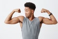 Close up of young athletic handsome dark-skinned man with afro hairstyle in sporty grey shirt looking at his muscles Royalty Free Stock Photo