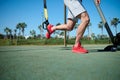 Close-up young athletic man in sports clothing training legs with fitness suspension straps in the outdoors sportsground