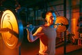 Close up young athletic man training with barbell in gym in mixed neon light. Royalty Free Stock Photo