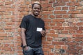 Dark-skinned man in T-shirt showing blank business card on bricked background. Royalty Free Stock Photo
