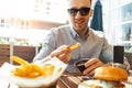 Close up of young attractive man eating french fries and burger at street cafe. Royalty Free Stock Photo