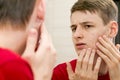 Close up of young attractive man with problematic skin and scars from acne looks in the mirror in the bathroom