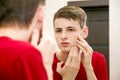 Close up of young attractive man with problematic skin and scars from acne looks in the mirror in the bathroom