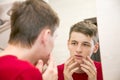 Close up of young attractive man with problematic skin and scars from acne looks in the mirror in the bathroom