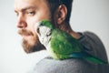 Close-up of young beard man with his pet Quaker parrot on shoulder at home. Royalty Free Stock Photo