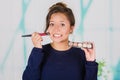 Close up of young beautiful woman holding a make up palette and doing crazy make-up in her face using a brush, in a