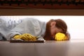 Close up of young beautiful woman with yellow rubber gloves and rag is cleaning floor under bed at home. Concept of Royalty Free Stock Photo