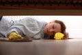 Close up of young beautiful woman with yellow rubber gloves and rag is cleaning floor under bed at home. Concept of Royalty Free Stock Photo