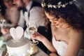 A close-up of a young bride sitting at a table on a wedding, holding a glass of wine.