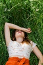 Close up of young brunette girl in white top and red skirt lying down in green meadow field grass in countryside Royalty Free Stock Photo