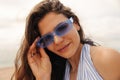 Close-up young caucasian girl puts on blue modern sunglasses and looking at camera. Royalty Free Stock Photo