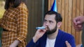 Close-up young Caucasian man tired of celebrating birthday party with friends, wearing funny hat and blowing whistle.