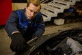 Close-up of a young Caucasian mechanic in car service adjusting headlights on car in the repair shop garage. Auto service, car Royalty Free Stock Photo