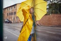 Close-up of a young cheerful woman with a yellow raincoat and umbrella who is in a good mood while walking the city on a rainy day Royalty Free Stock Photo