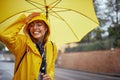 Close-up of a young cheerful woman with a yellow raincoat and umbrella who is in a good mood while walking the city on a rainy day Royalty Free Stock Photo