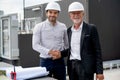 Close up young engineer shake hands with senior coworker and stay in front of line of air vent in construction site to express Royalty Free Stock Photo