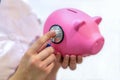 Close-up of a young female Doctor in a white medical coat Holding a cute pink piggy Bank and checking it with a stethoscope on a w Royalty Free Stock Photo
